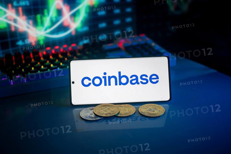 Coinbase logo on smartphone with coins, blue neon lights, and trading charts in background