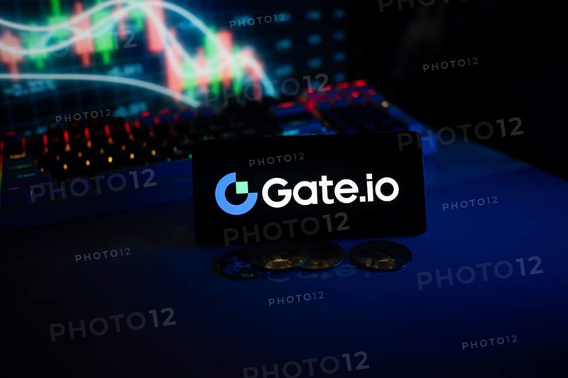 Gate.io logo displayed on a phone with cryptocurrency coins and market charts
