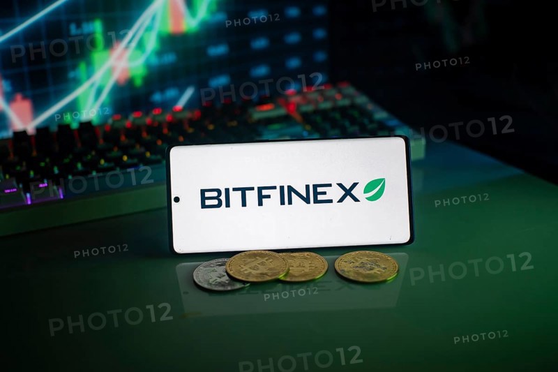 Bitfinex logo on a smartphone with cryptocurrencies and financial trading graphs behind