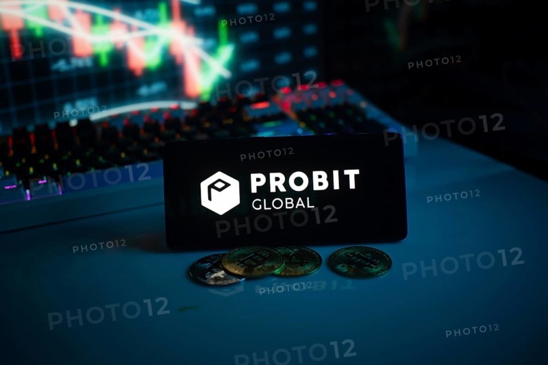 Probit Global logo with coins on a desk, against trading graphs backdrop