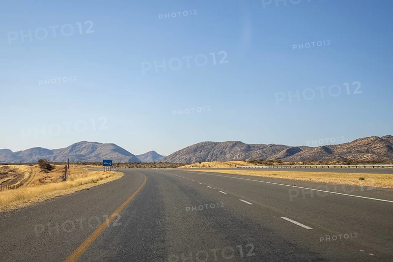 Scenic view of the open road between Windhoek and Outjo, surrounded by dry grasslands and distant mountains under a clear blue sky