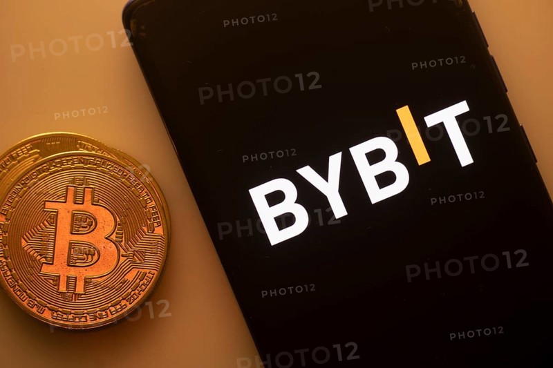 Bybit logo on a black smartphone beside a Bitcoin on an orange background