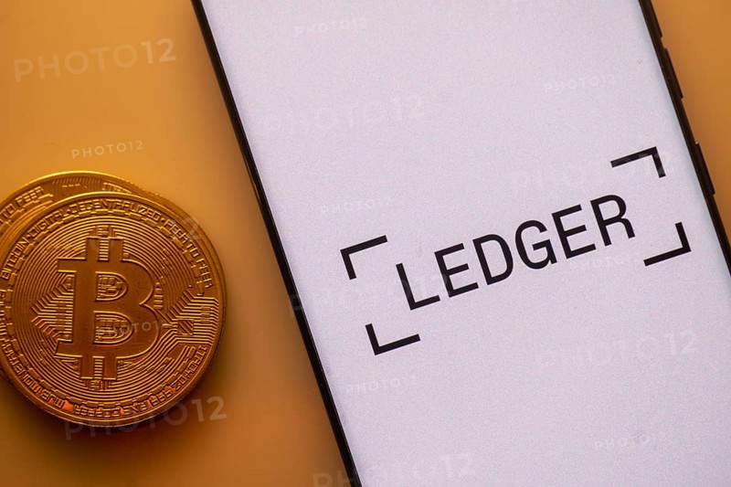 Bitcoin displayed next to a smartphone with Ledger app interface on white background