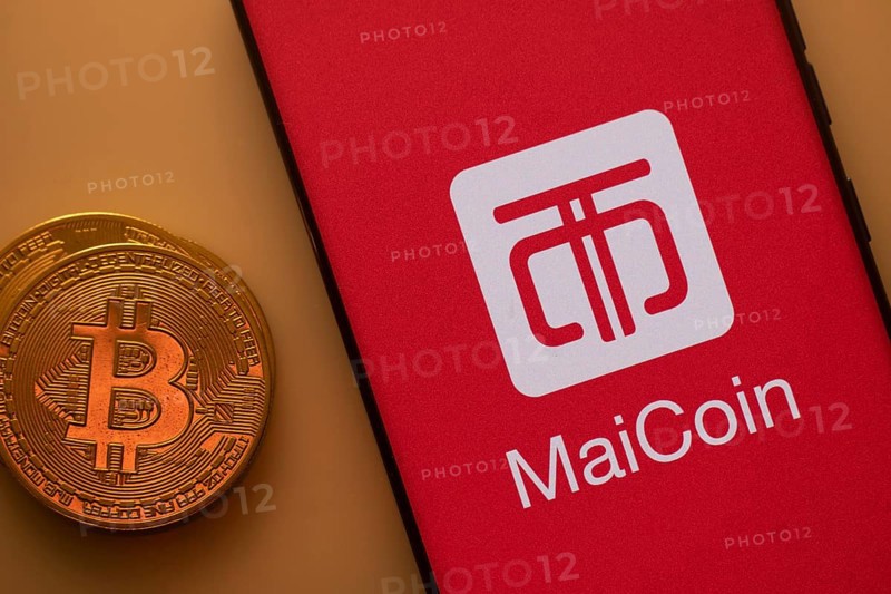 Bitcoin coin next to a smartphone featuring the MaiCoin logo on a red background