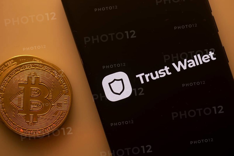 Bitcoin coin near a phone displaying Trust Wallet logo on a black screen