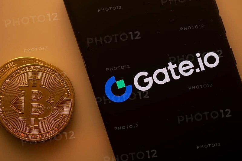 Bitcoin coin adjacent to a phone with the Gate.io logo on a black screen