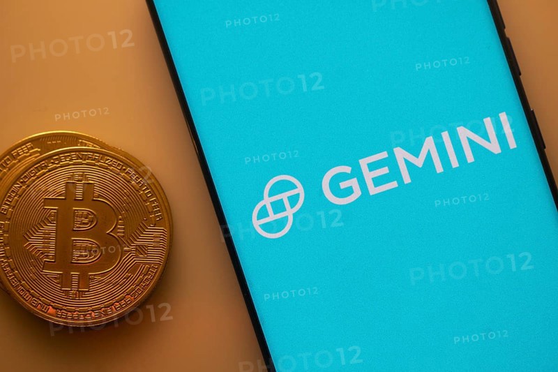 Gemini logo on a smartphone screen alongside a Bitcoin coin