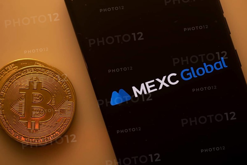 Bitcoin coin beside phone showing MEXC Global logo on a black background