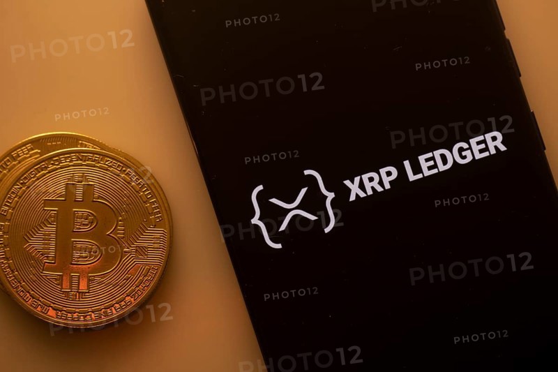 Bitcoin coin next to a phone displaying XRP Ledger logo on a black background