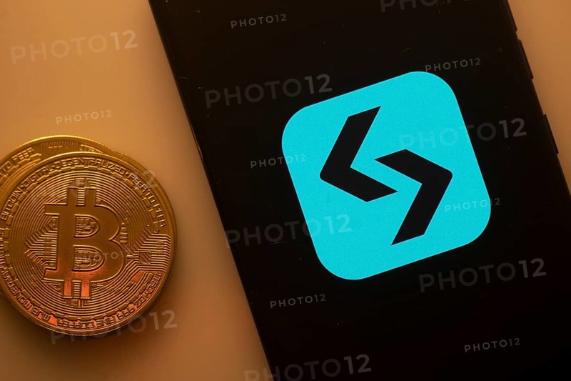 Unidentified logo on smartphone beside Bitcoin, emphasizing cryptocurrency and blockchain technology