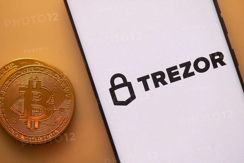 Trezor logo on phone beside Bitcoin, highlighting cryptocurrency security and storage solutions