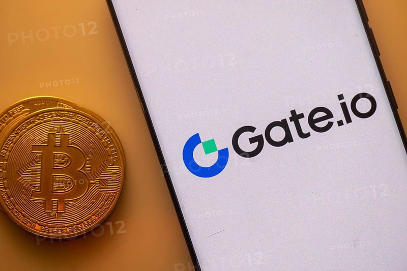 Gate.io logo on a smartphone screen next to a Bitcoin standing on an orange backdrop