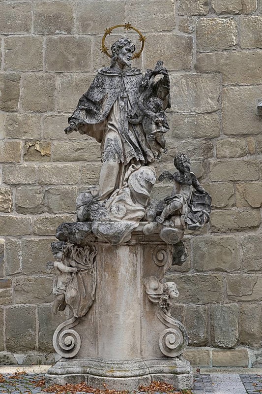 Baroque stone statue of a saint with angel on a decorated pedestal in front of a stone wall, parish church St.Stephan Tulln Lower Austria Austria