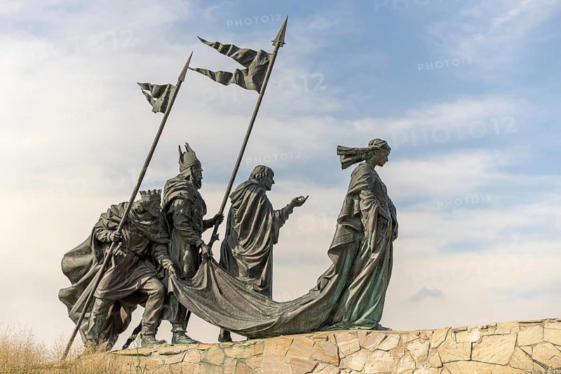 Sculpture group of historical figures with flags on a stone platform under a blue sky, Nibelungendenkmal Minoritenplatz Tulln Lower Austria Austria