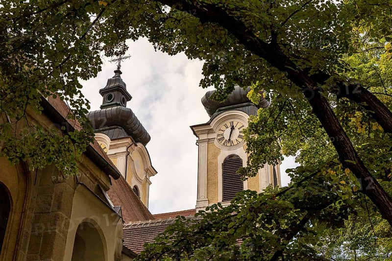 Baroque church towers with clocks, surrounded by deciduous trees under a cloudy sky, parish church St.Stephan Tulln Lower Austria Austria
