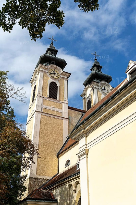 Baroque church towers with clocks rise against a clear blue sky in the afternoon light, St.Stephan parish church Tulln Lower Austria Austria