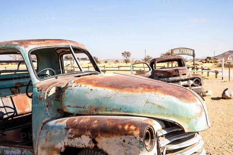 Solitaire's car graveyard in Namibia features rusted vintage cars near small desert buildings, set against dunes and mountains, capturing desert charm and isolation