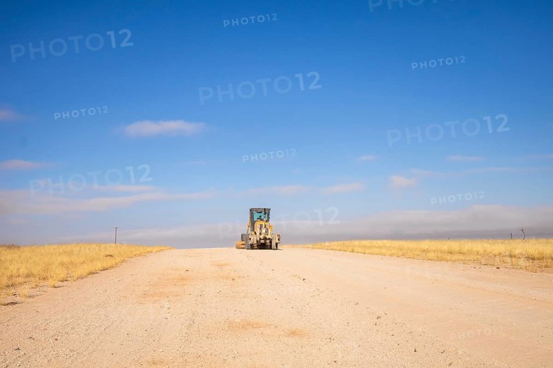 In the remote desert near Solitaire, Namibia, a tractor levels a dirt road across golden sand dunes and rugged desert terrain