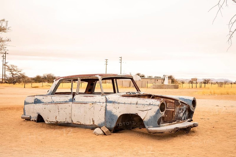 Solitaire's car graveyard in Namibia features rusted vintage cars near small desert buildings, set against dunes and mountains, capturing desert charm and isolation