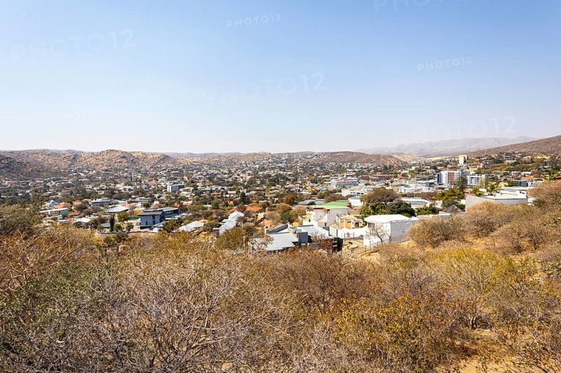 A panoramic view of Windhoek, Namibia, from the National Botanic Garden, showing the city's mix of homes, modern buildings, and a distant church framed by dry hills and mountains