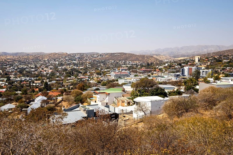 A panoramic view of Windhoek, Namibia, from the National Botanic Garden, showing the city's mix of homes, modern buildings, and a distant church framed by dry hills and mountains