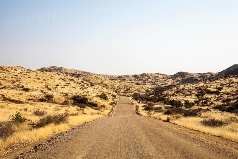 A road Spreetshoogte Pass in Namibia, with a gravel road winding through golden grassland and rocky hills under a bright, clear sky