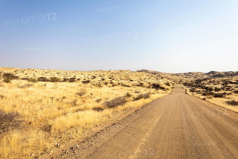 A road Spreetshoogte Pass in Namibia, with a gravel road winding through golden grassland and rocky hills under a bright, clear sky