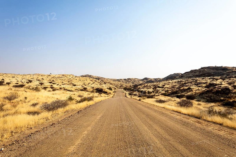 A road Spreetshoogte Pass in Namibia, with a gravel road winding through golden grassland and rocky hills under a bright, clear sky