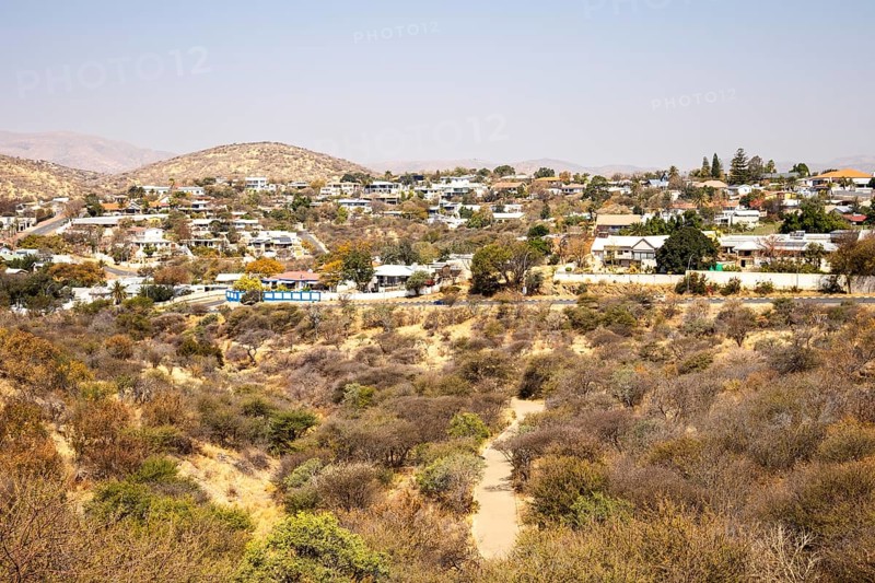 A panoramic view of Windhoek, Namibia, from the National Botanic Garden, showing the city's mix of homes, modern buildings, and a distant church framed by dry hills and mountains