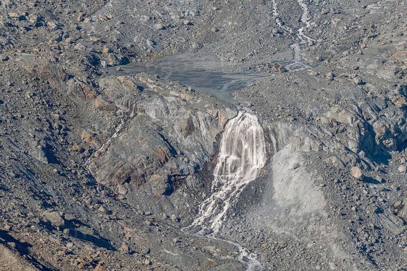 Waterfalls flow over a glacier surrounded by rocks and debris. This natural phenomenon is caused by the melting of ice, which can be observed on a sunny day. Gorner Glacier, Zermatt, Valais, Alps, Swiss