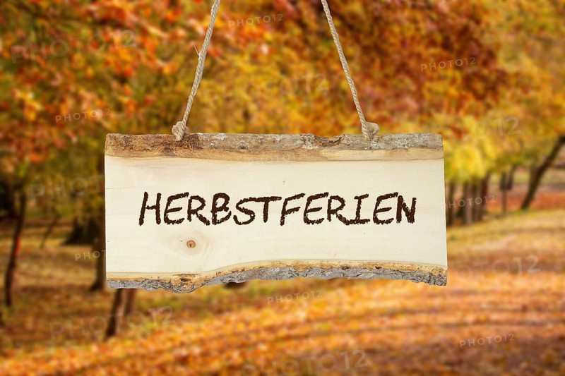 (photomontage) : Wooden sign with the inscription HERBSTFERIEN in front of an autumn-coloured deciduous forest