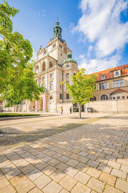 Mesmerising building surrounded by spring trees under a blue sky and paved area, Munich, Germany