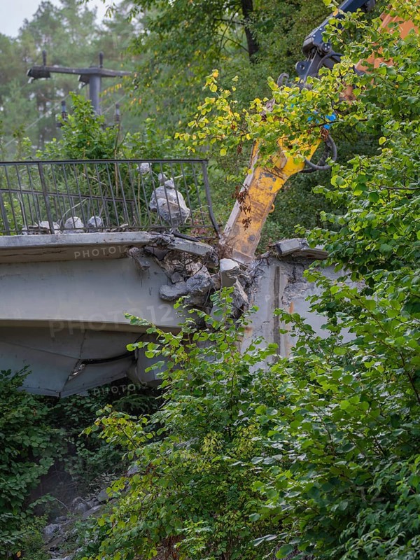 An excavator working on the end of a bridge, surrounded by dense greenery, bridge demolition, Calw, Germany