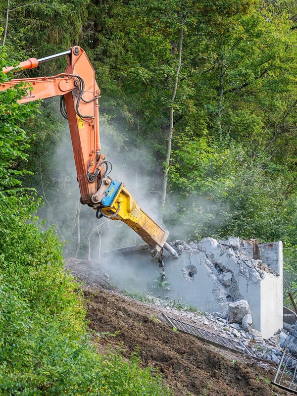 An excavator breaks a concrete wall in a green environment, dust rises, bridge demolition, Calw, Germany