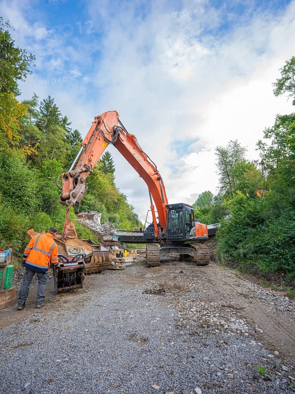 A worker and an excavator carry out work on a road covered with gravel, bridge demolition, Calw, Germany
