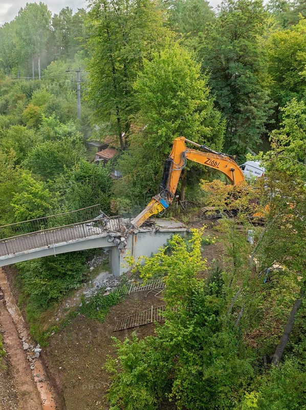 Excavator tears down part of a bridge in a green forest, an empty path runs underneath, bridge demolition, Calw, Germany