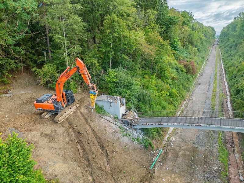 An excavator demolishes a bridge next to railway tracks in the forest, bridge demolition, Calw, Germany