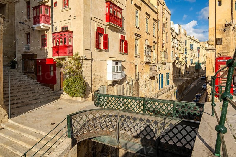 Street with incredible historic houses with colorful wooden balconies in La Valletta, capital city of Malta, bridge of Victoria Gate