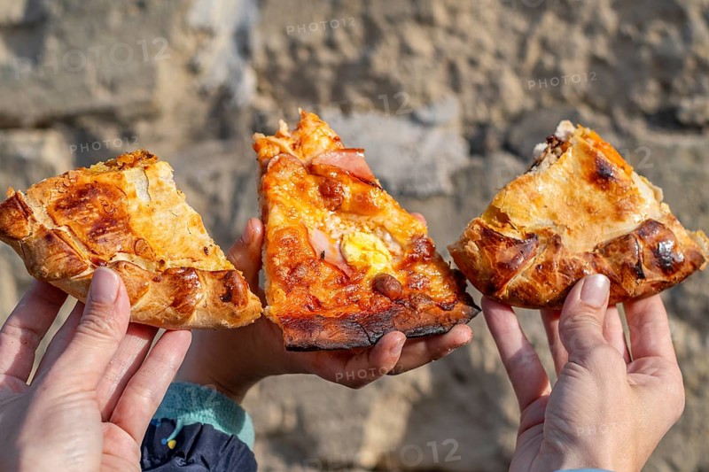 Three slices of maltese pizza hold in the hands of mother and son with stone background, Gozo, Malta