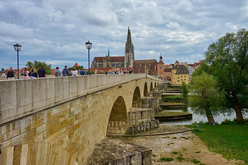 People walking across a historic bridge with a view of the cathedral and trees, Stone Bridge, Danube, Regensburg, Bavaria, Germany