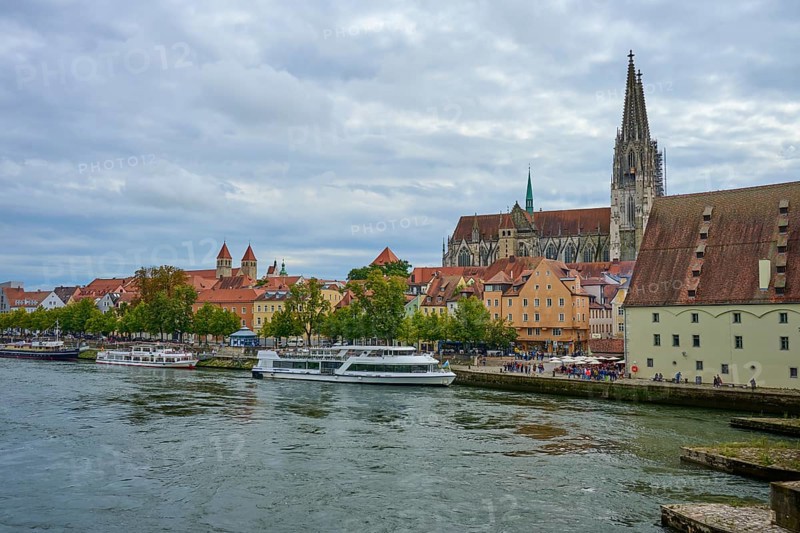 View of a cathedral and boats on a riverbank on a slightly cloudy day, Danube, Regensburg, Bavaria, Germany