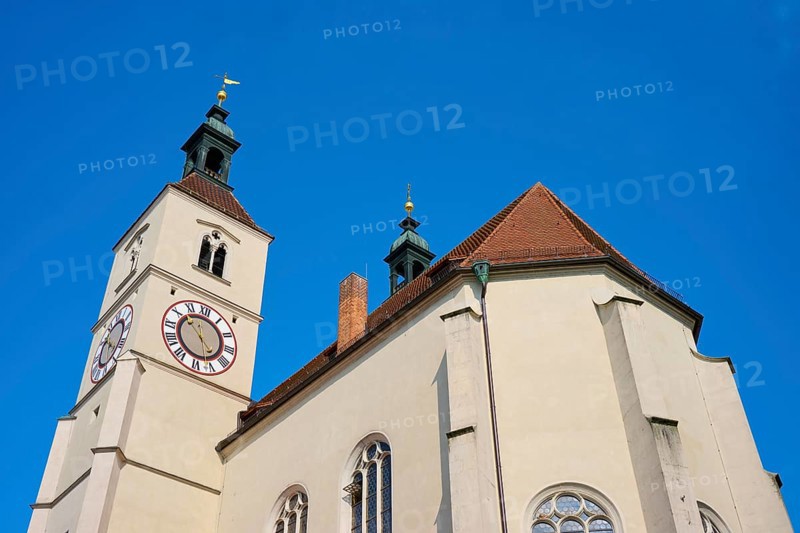 Close-up of a church tower with clock and red tiled roofs against a deep blue sky, Neupfarrkirche, Regensburg, Bavaria, Germany