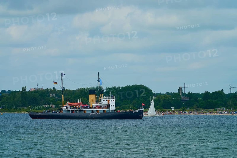 Historic icebreaker Stettin and a small sailing boat in front of a green coastal landscape and cloudy sky, Windjammer Parade Kiel 2025, Heikendorf, Plön district, Kiel Fjord, Schleswig-Holstein, Germany