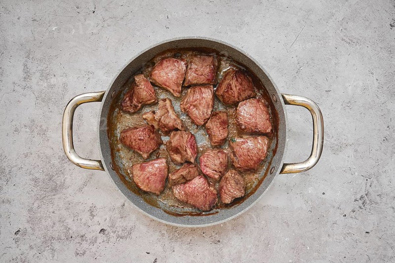 Chunks of beef are sizzling in a frying pan, showcasing a delicious golden-brown crust in the kitchen countertop