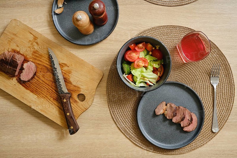 Slices of succulent duck breast are laid out on a cutting board beside a vibrant salad filled with tomatoes and lettuce. A refreshing drink sits nearby, creating an inviting dining experience