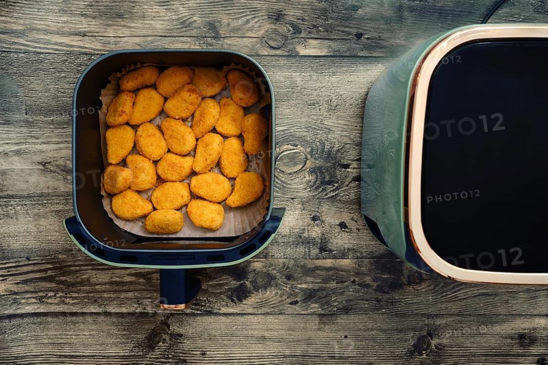 Crispy chicken nuggets cooking in an air fryer on a wooden kitchen table