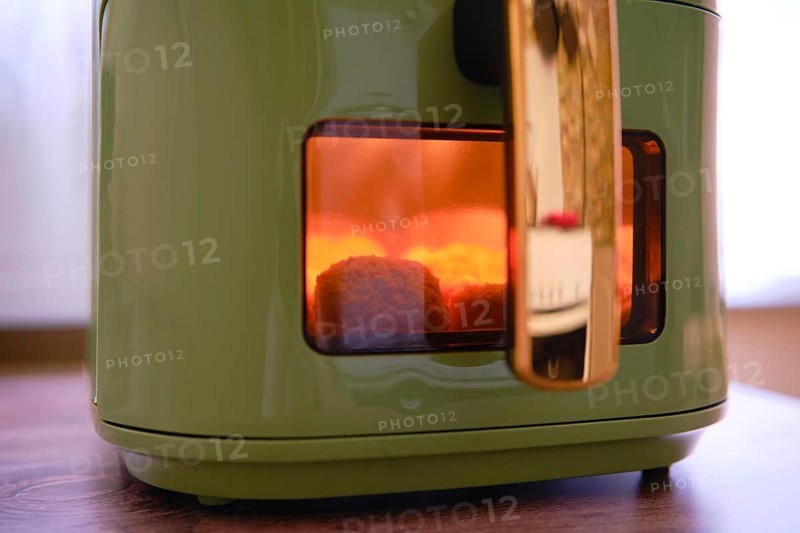Golden-brown chicken nuggets are cooking in an air fryer, with a warm glow visible through the glass window. The cozy atmosphere suggests a leisurely afternoon meal preparation at home