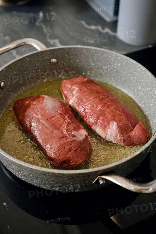 Two duck breasts are sizzling in a pan with hot fat, infusing the kitchen with rich aroma