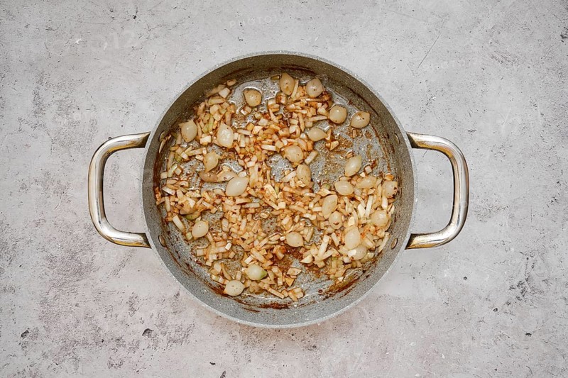 A silver pan contains a mixture of caramelized pearl onions and chopped shallot, creating a savory aroma in the kitchen. The onions are golden brown, indicating a rich flavor