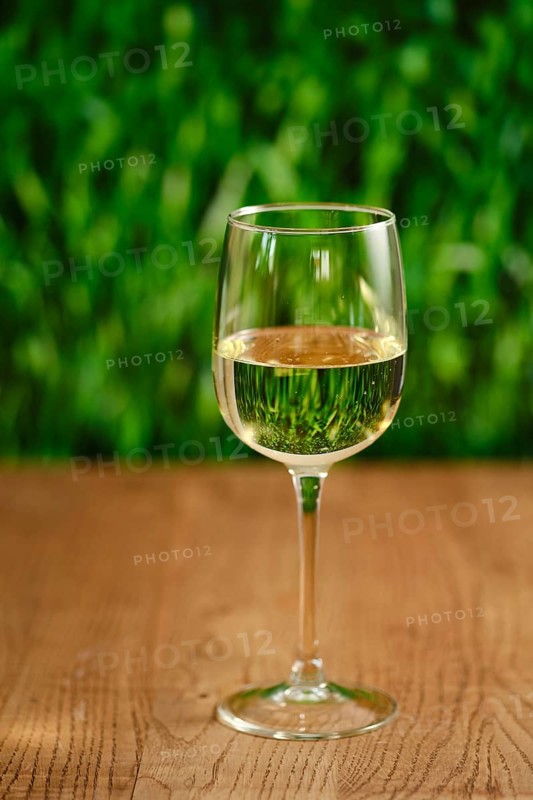 A clear glass filled with white wine sits on a smooth wooden table. The soft green background creates a calming atmosphere, perfect for relaxation and social gatherings